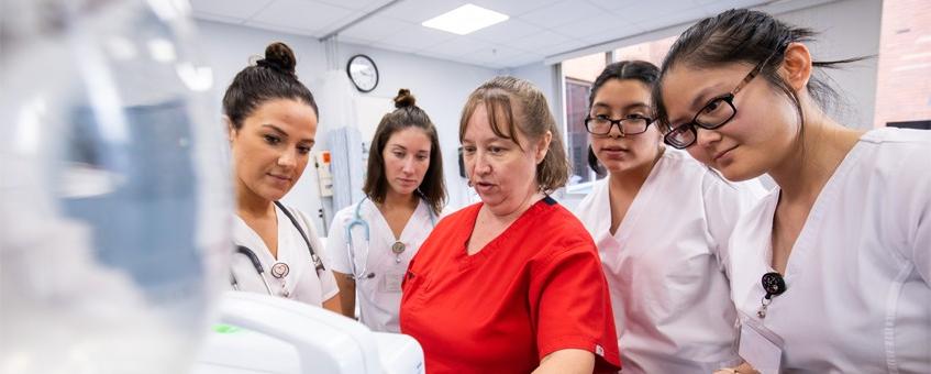 A group of Nursing students surrounding their instructor while all look at a computer screen.