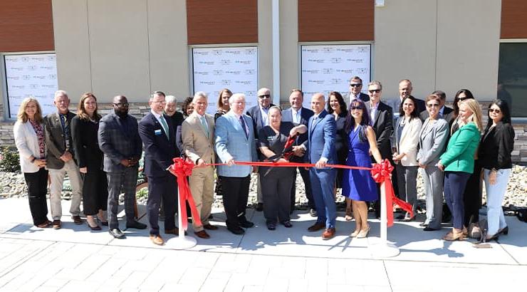 A large group of people at the Highmark Center of Excellence Ribbon Cutting standing in front of a long red ribbon